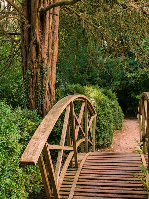A narrow, ascending pathway in a residential garden in St Johns Wood, with a stone and brick retaining wall on the right side, featuring a metal handrail. The pathway is composed of wooden steps leadi